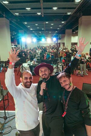 Three men smiling and waving at the crowd during a live performance murdah srvc photo