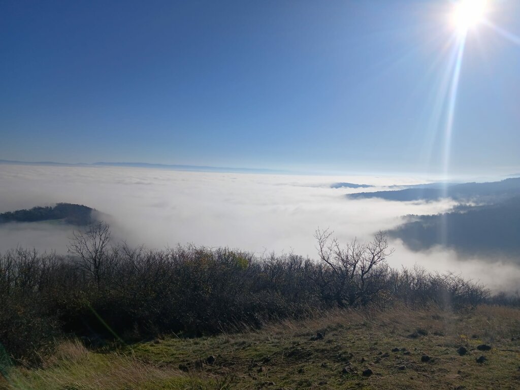 eyJlbiI6IkEgcGFub3JhbWljIHZpZXcgYWJvdmUgYSBzZWEgb2YgY2xvdWRzLCByZXZlYWxpbmcgdGhlIHZvbGNhbmljIHBlYWtzIG9mIHRoZSB0ZXJyb2lyIGJlbmVhdGggYSBicmlsbGlhbnQgc3VuIiwiZnIiOiJWdWUgcGFub3JhbWlxdWUgYXUtZGVzc3VzIGQndW5lIG1lciBkZSBudWFnZXMsIGTpdm9pbGFudCBsZXMgc29tbWV0cyBkZXMgcmVsaWVmcyBkdSB0ZXJyb2lyIHZvbGNhbmlxdWUgc291cyB1biBzb2xlaWwg6WNsYXRhbnQuIn0=