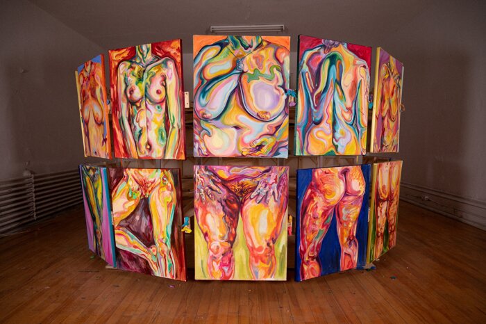 Large-scale immersive art installation by Valentine Alma, Montreal-based artist in Quebec, featuring a circular structure composed of multiple vibrant abstract painted panels with swirling patterns and expressive human body forms in bold colors such as red, yellow, blue, and pink, displayed in a contemporary gallery space with wooden floors and soft ambient lighting