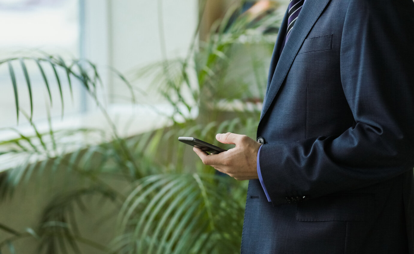 male-office-worker-suit-with-smartphone-near-window-palm-trees.jpeg