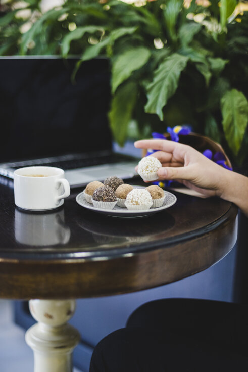 close-up-person-s-hand-chocolate-balls-with-coffee-laptop-round-wooden-table.jpeg