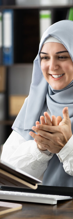 Frau mit Kopftuch, die in ein Notebook blickt und erfreut aussoieht. 