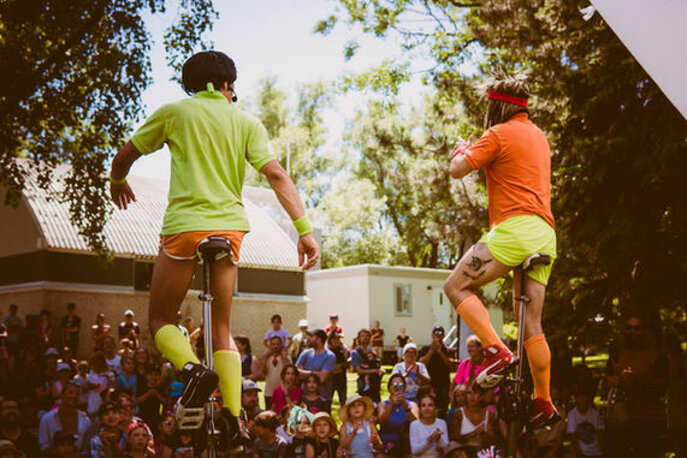 Deux artistes de cirque Nacho Salsa sur monocycles devant une grande foule en plein air, en tenue de tennis verte et orange