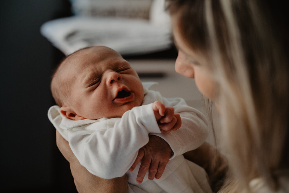 Newborn Photography, bambino neonato tra le braccia della sua mamma. Il bimbo sta sbadigliando assonnato.